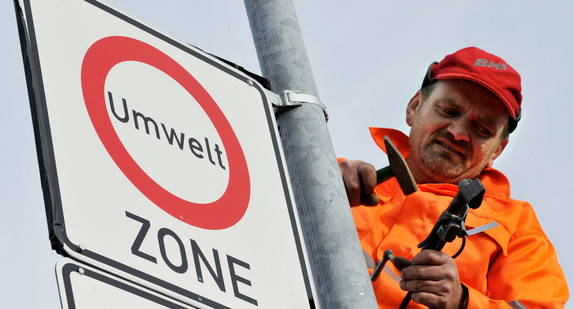 Ein Mitarbeiter einer Straßenschilderfirma befestigt in Freiburg ein Verkehrsschild, das auf eine Umweltzone in der Innenstadt hinweist (Bild: dpa).