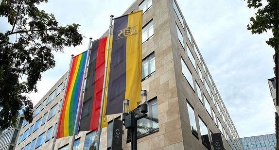 Vor dem Gebäude des Sozialministerium hängen nebeneinander eine Regenbogenflagge sowie die Flaggen von Deutschland und Baden-Württemberg.