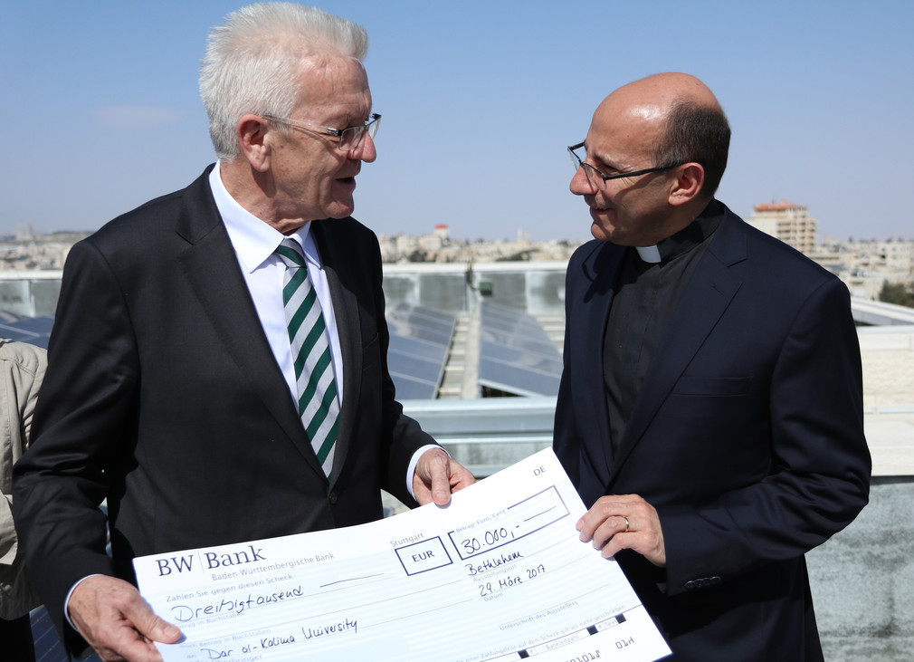 Ministerpräsident Winfried Kretschmann (l.) übergibt Pfarrer Mitri Raheb (r.) beim Besuch des Dar al-Kalima College in Bethlehem einen Scheck zum Ausbau der Solaranlage des Colleges