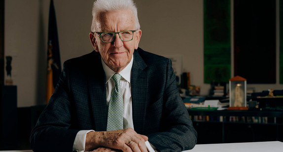 Ministerpräsident Winfried Kretschmann sitzt am Schreibtisch.