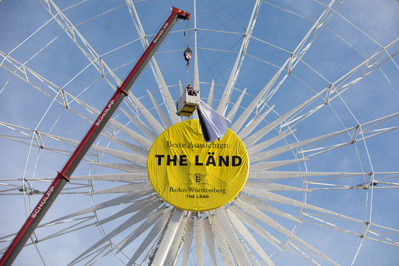 Riesenrad auf dem Stuttgarter Schlossplatz mit der Aufschrift „Beste Aussichten: THE LÄND“ und dem Landeswappen