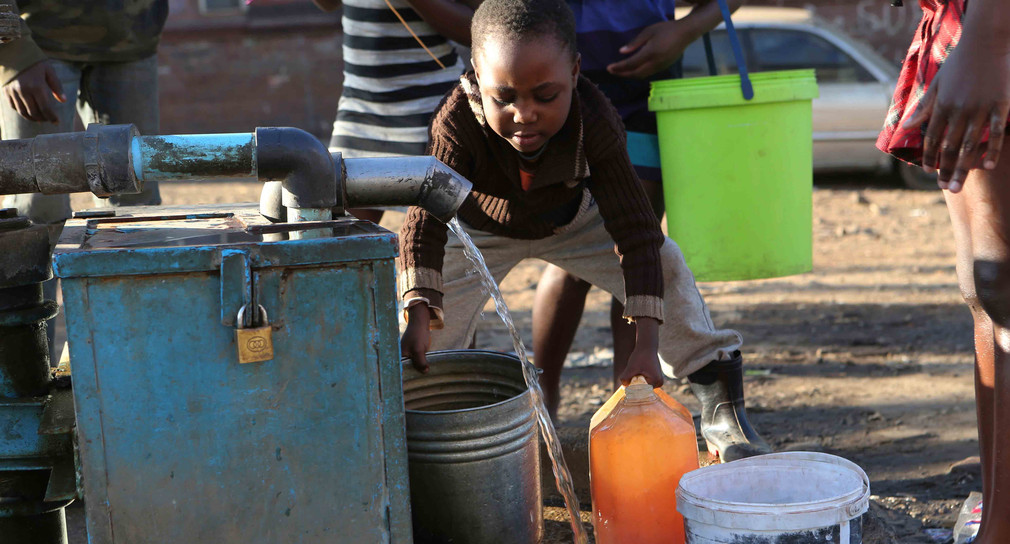 Ein Kind füllt einen Eimer mit Wasser auf.