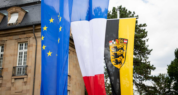 An Fahnemasten hängen die Fahne der EU, die französische Fahne und die baden-württembergische Fahne.