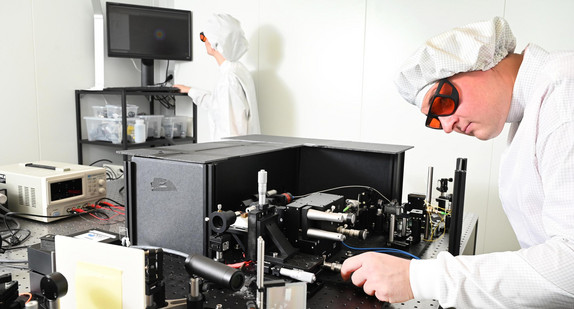 In einem Labor der Firmja Q.ANT wird von einer Ingenieurin und einem Ingenieur der Test eines neuentwickelten photonischen Chips mit einem Laserstrahl vorbereitet.