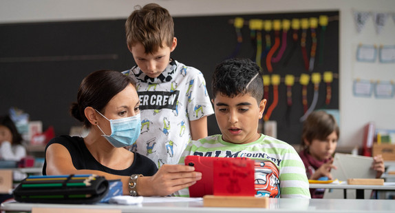 Eine Lehrerin mit Mundschutz gibt zwei Schülern einer Grundschule im Rahmen der sogenannten "Lernbrücken" Nachhilfe.