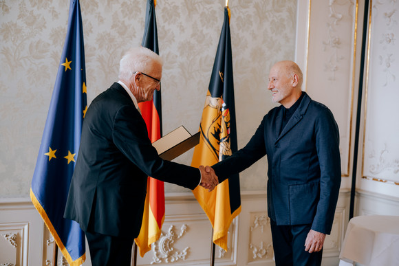 Ministerpräsident Winfried Kretschmann (links) und Tadeusz Matacz (rechts) stehen vor Fahnen und geben sichc die Hand..