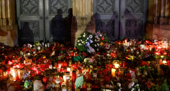 Schatten Anteilnehmender sind am Portal des Magdeburger Doms zu sehen. Davor liegen Kränze, Blumen und Kerzen.