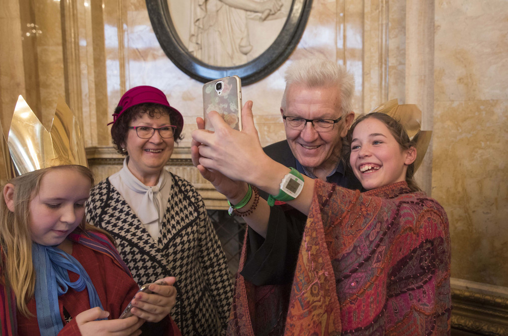 Eine Sternsingerin macht ein Selfie mit Ministerpräsident Winfried Kretschmann (2.v.r.).