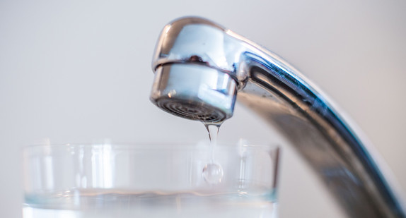 Wasser läuft aus einem Wasserhahn in ein Glas.