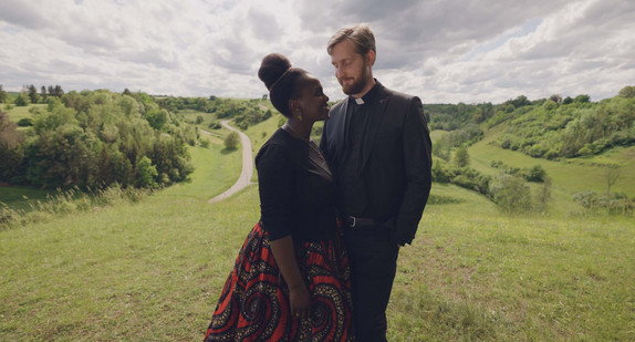 Standbild aus der SWR-Spielfilmproduktion „Baden gegen Württemberg“: ein Priester und eine Frau in einer Landschaft.