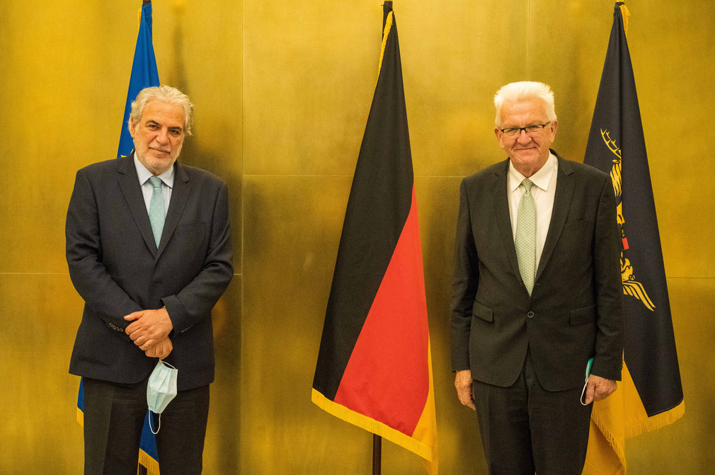 Ministerpräsident Winfried Kretschmann (r.) und Christos Stylianides (l.) stehen vor Fahnen.