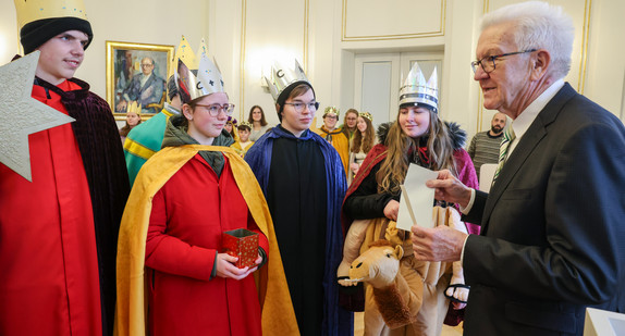 Ministerpräsident Winfried Kretschmann (rechts) überreicht Sternsingerinnen und Sternsingern einen Umschlag.