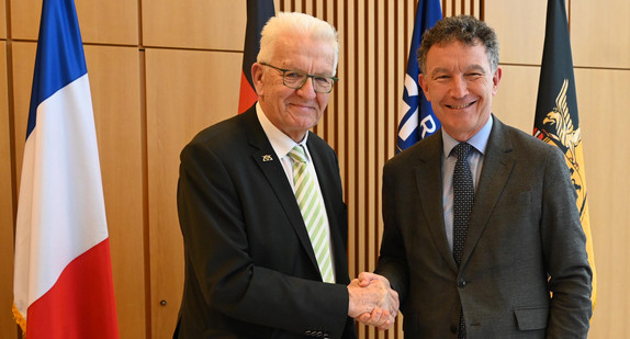 Ministerpräsident Winfried Kretschmann (links) und Franck Leroy (rechts), Präsident der Region Grand Est, stehen vor Fahnen und geben sich die Hand.