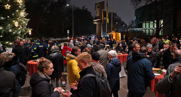 Gäste der Weihnachtsbaum-Übergabe stehen an Stehtischen, unterhalten sich und genießen bei winterlichen Temperaturen Glühwein, Punk und Bratwürste