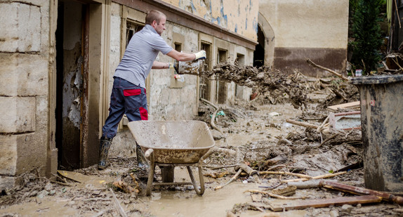 Ein Mann schüttet bei Aufräumarbeiten nach einem schweren Unwetter in Braunsbach Schlamm aus einem Haus (Bild: © dpa).