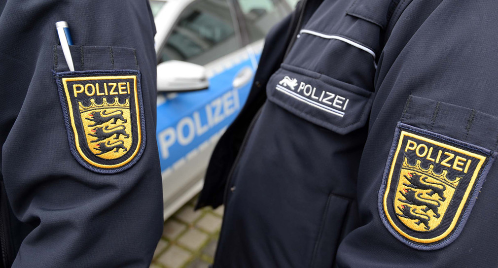 Zwei Wappen der baden-württembergischen Polizei sind neben einem Polizeifahrzeug zu sehen.