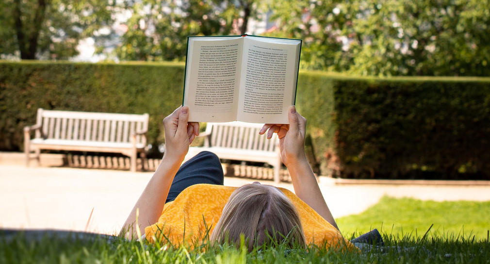 Eine Person liegt auf der Wiese im Park der Villa Reitzenstein und liest ein Buch.