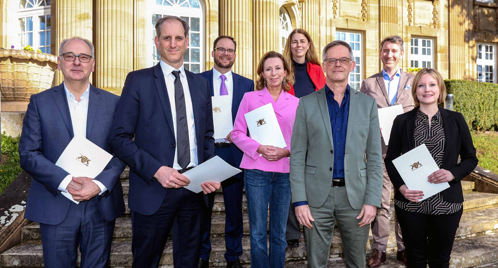 von links nach rechts: Prof. Dr. Hans-Peter Welte, LFK-Präsident Dr. Wolfgang Kreißig, Prof. Christof Seeger, Stefanie Knecht, Arnhilt Kuder, Staatssekretär Rudi Hoogvliet, Prof. Dr. Boris Alexander Kühnle und Sabrina Hartmann stehen auf der Treppe vor der Villa Reitzenstein. 