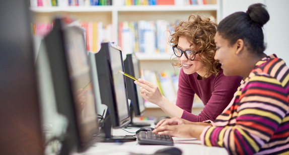 Zwei junge Frauen zeigen auf den Monitor und diskutieren gemeinsam über die Präsentation am Computer.