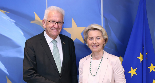 Ministerpräsident und Kommissionspräsidentin stehen vor einer Flagge der Europäischen Union.