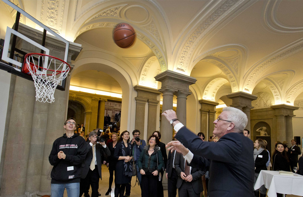 Ministerpräsident Winfried Kretschmann (r.) wirft einen Basketball.