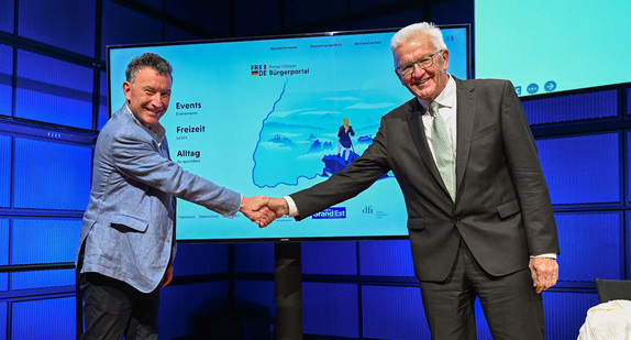 Ministerpräsident Winfried Kretschmann (rechts) und der Präsident der Région Grand Est, Franck Leroy (links), geben sich vor einer Videowand mit dem neuen Bürgerportal die Hand.