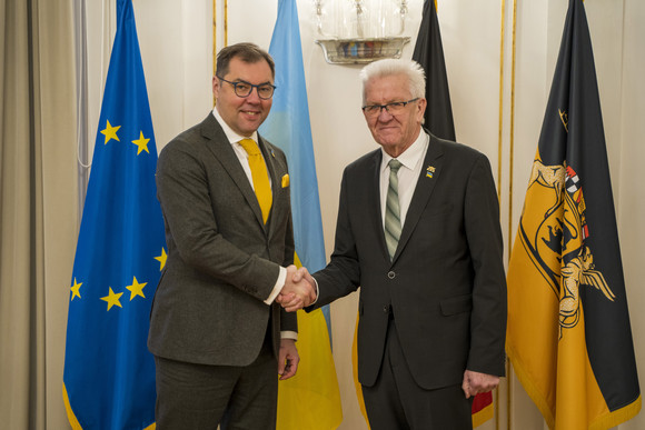 Ministerpräsident Winfried Kretschmann (r.) und der ukrainische Botschafter Oleksii Makeiev (l.) stehen in der Villa Reitzenstein vor Fahnen und geben sich die Hand.