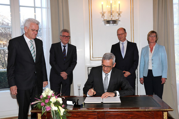 Staatssekretär Martin Jäger (sitzend) unterzeichnet die Vereinbarung; stehend v.l.n.r.: Ministerpräsident Winfried Kretschmann, Volker Stich, Vorsitzender des Beamtenbundes Baden-Württemberg, , Matthias Grewe, Vorsitzender des Vereins der Richter und Staatsanwälte Baden-Württemberg e.V., und Finanzministerin Edith Sitzmann