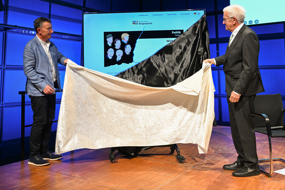 Ministerpräsident Winfried Kretschmann (rechts)  und der Präsident der Région Grand Est, Franck Leroy (links), enthüllen eine Videowand mit dem neuen Bürgerportal