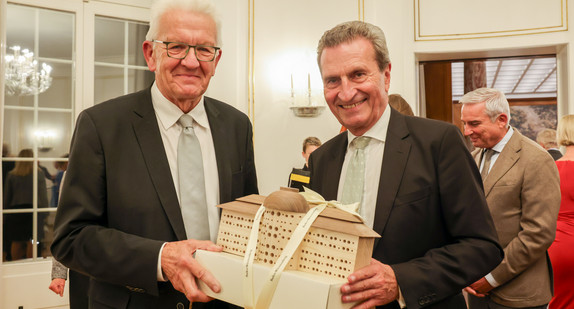 Ministerpräsident Winfried Kretschmann (links) überreicht dem ehemaligen Ministerpräsidenten Günther Oettinger (rechts) bei einem Empfang anlässlich dessen 70. Geburtstages ein Bienenhotel in Form der Villa Reitzenstein.
