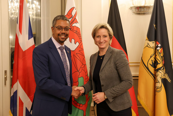 Wirtschaftsministerin Dr. Nicole Hoffmeister-Kraut (rechts) und der walisische Wirtschaftsminister Vaughan Gething (links) stehen vor Fahnen und geben sich die Hand.