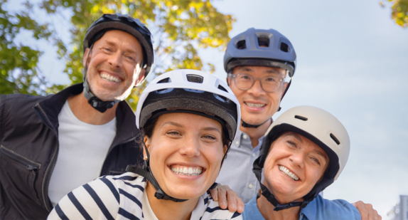Vier Menschen stehen lächeld da und tragen Fahrradhelme.