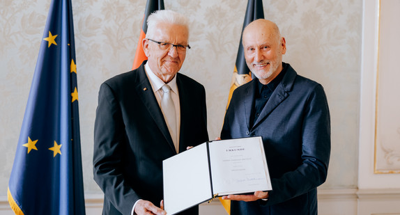 Ministerpräsident Winfried Kretschmann (links) und Tadeusz Matacz (rechts) stehen vor Fahnen und präsentieren die Verleihungsurkunde.
