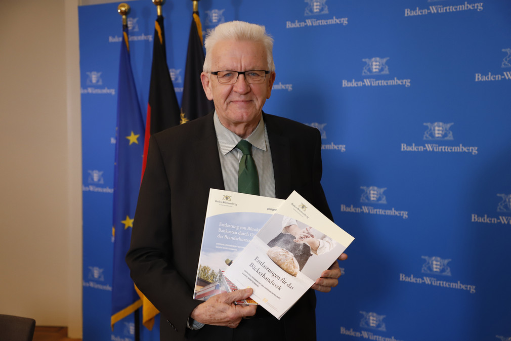 Ministerpräsident Winfried Kretschmann mit zwei Empfehlungsberichten des Normenkontrollrats Baden-Württemberg zu Möglichkeiten des Bürokratieabbaus im Bäckerhandwerk und beim Brandschutz