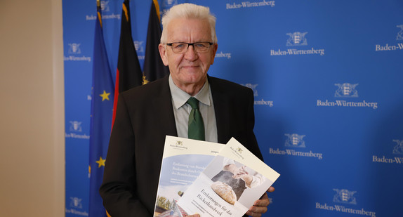 Ministerpräsident Winfried Kretschmann mit zwei Empfehlungsberichten des Normenkontrollrats Baden-Württemberg zu Möglichkeiten des Bürokratieabbaus im Bäckerhandwerk und beim Brandschutz