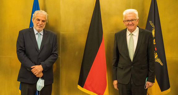 Ministerpräsident Winfried Kretschmann (r.) und Christos Stylianides (l.) stehen vor Fahnen.