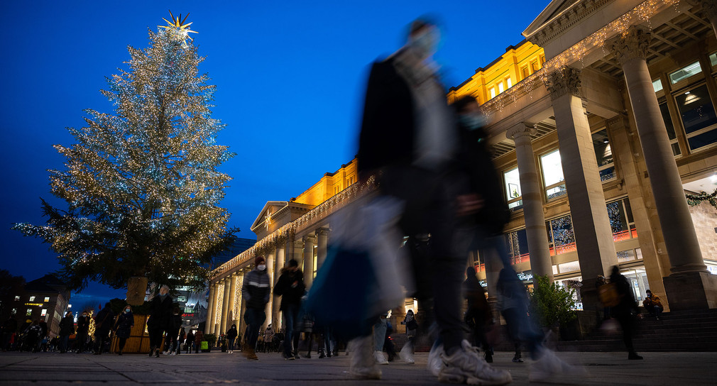 Passanten gehen über den weihnachtlich beleuchteten Schlossplatz in Stuttgart. 