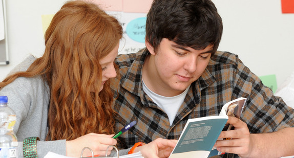 Eine Schülerin und ein Schüler lesen gemeinsam einen Text (Bild: © dpa).