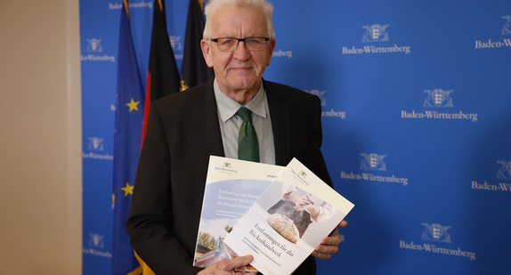 Ministerpräsident Winfried Kretschmann mit zwei Empfehlungsberichten des Normenkontrollrats Baden-Württemberg zu Möglichkeiten des Bürokratieabbaus im Bäckerhandwerk und beim Brandschutz