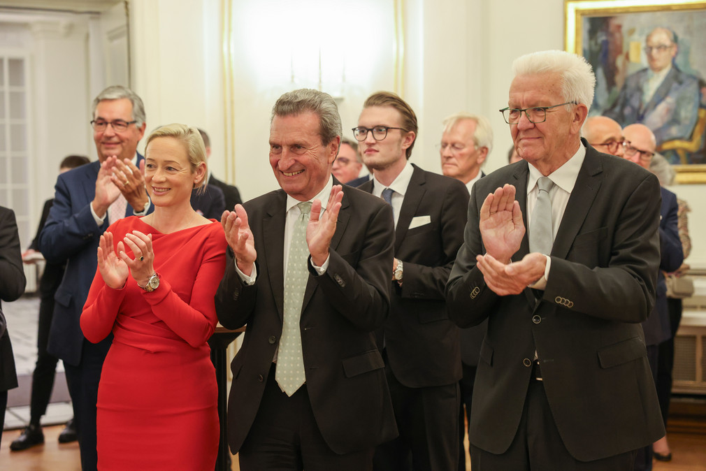 von links nach rechts (vorne): Friederike Beyer, der ehemalige Ministerpräsident Günther H. Oettinger und Ministerpräsident Winfried Kretschmann stehen im Runden Sall der Villa Reitzenstein und applaudieren.