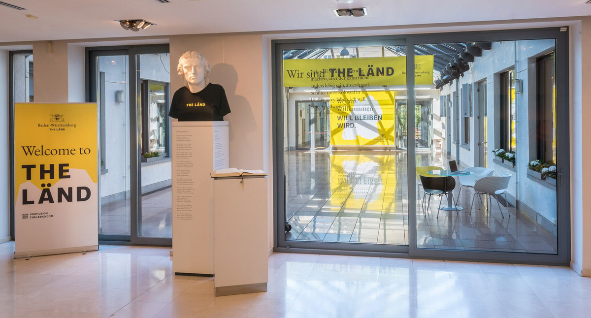 Blick vom Foyer mit Schillerbüste in das glasüberdachte Patio mit „THE LÄND“.