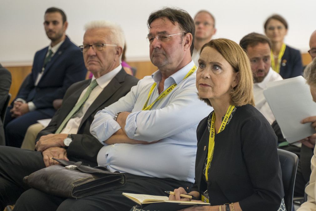 Ministerpräsident Winfried Kretschmann (links) und Wissenschaftsministerin Petra Olschowski (rechts) als Zuhörer bei einem Vortrag in Sevilla über Unternehmen und Projekte im Bereich Wasserstoff. 