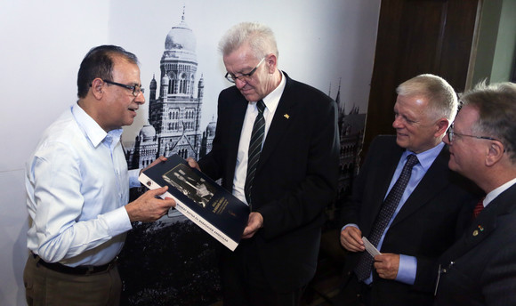 Der Verwaltungsdirektor der Stadt Mumbai, Municipal Commissioner Ajoy Mehta (l.), übergibt Ministerpräsident Winfried Kretschmann (M.) ein Buch.
