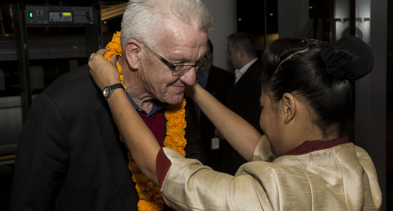 Eine Frau hängt Ministerpräsident Winfried Kretschmann zur Begrüßung in einem Hotel in Pune eine Kette um.