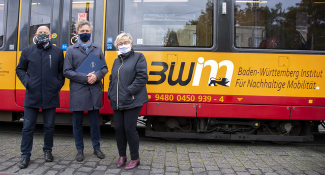 Verkehrsminister Hermann steht gemeinsam mit Oberbürgermeister Mentrup und Wissenschaftsministerin Bauer vor einer Straßenbahn mit der Aufschrift des BW Institut für nachhaltige Mobilität.']