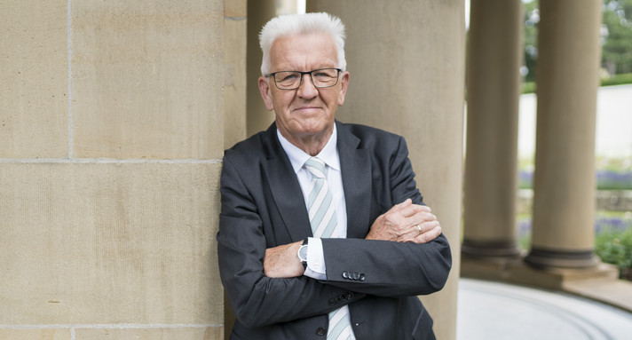 Beschreibung vom Bild: Man sieht Minister-Präsident Winfried Kretschmann. Er lehnt an einer Säule.