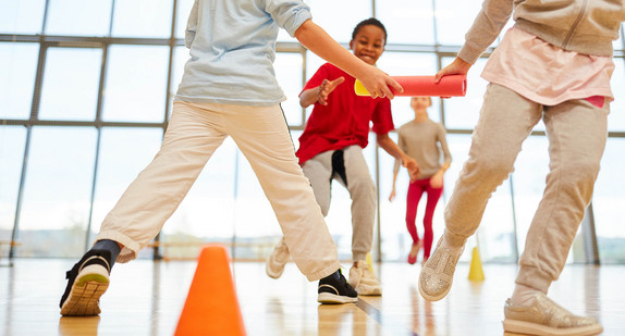 Ein Kinderteam macht einen Staffellauf im Sportunterricht in der Turnhalle.