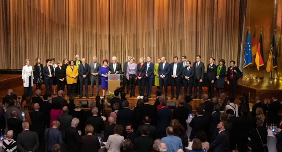 Ministerpräsident Winfried Kretschmann (Mitte) steht mit seiner Ehefrau Gerlinde und den Mitgliedern der Landesregierung auf der Bühne und spricht zu den Gästen.