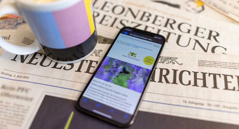 Ein Smartphone mit dem Newsletter von Baden-Württemberg.de liegt auf einer Zeitung.