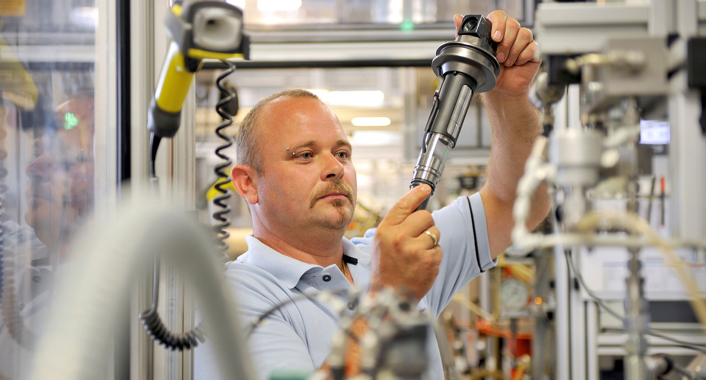 Ein Arbeiter in der Produktion prüft ein Bauteil. (Foto: © Bosch)']
